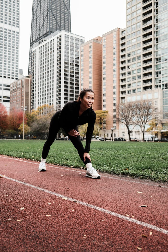 Asian woman stretching on a running track in urban Chicago with city skyscrapers in the background. Fitness and workout concept.